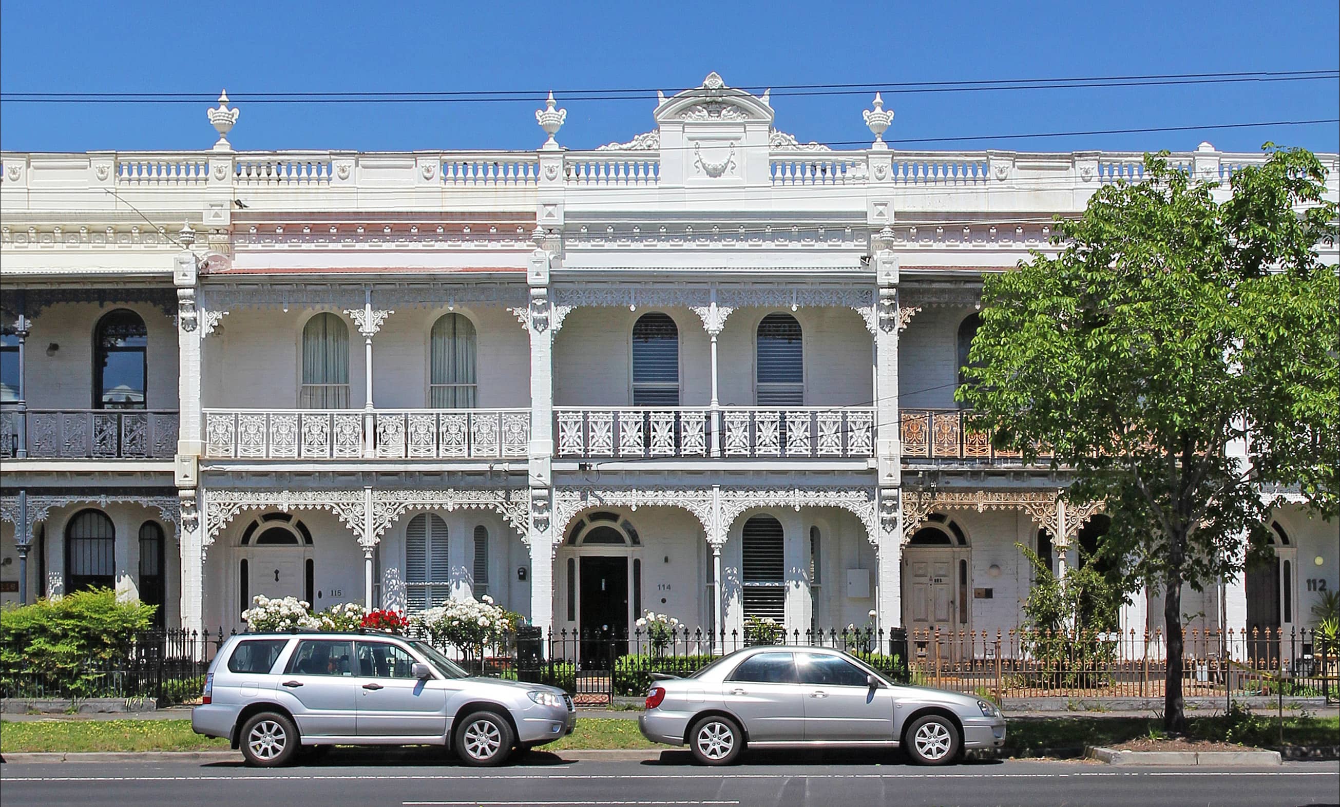 Cars lined up in front of elegant Victorian homes, showcasing classic architecture and a picturesque street scene.